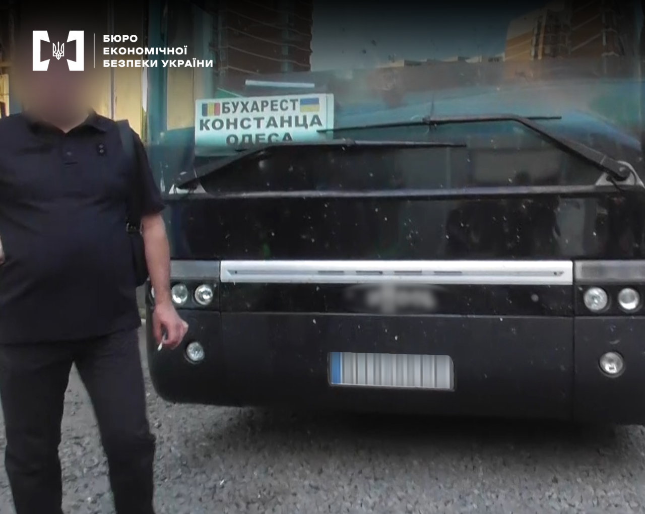 A black bus with a route sign reading 'Bucharest — Constanta — Odesa'. A man with a blurred face is standing nearby