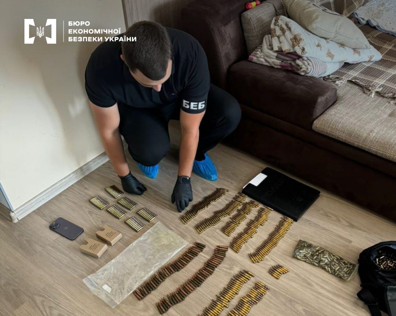 A ESBU detective in black gloves lays out a large number of seized rounds of ammunition on the floor of an apartment.