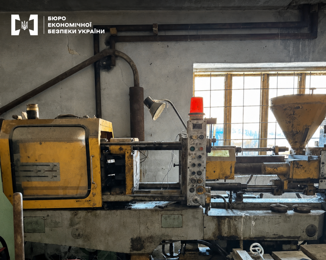 An industrial injection molding machine in a yellow and gray color scheme located inside an old production facility