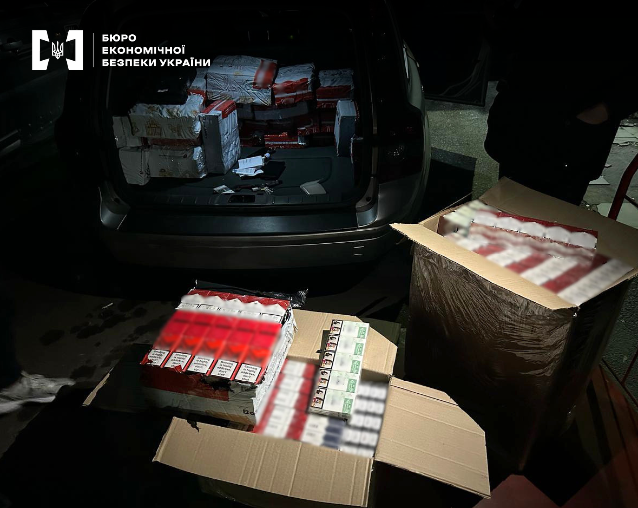 An open trunk of a car and boxes on the ground filled with cartons of smuggled cigarettes.