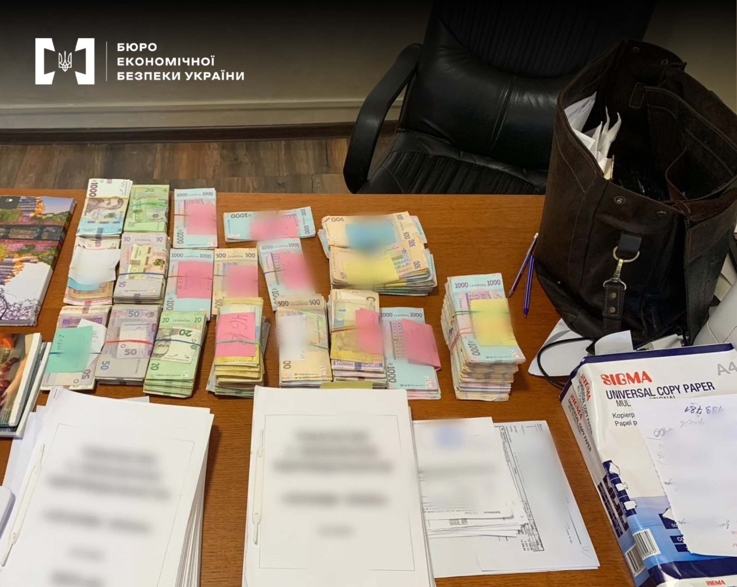 Stacks of bundles of hryvnias of various denominations and blurred document forms lie on a table