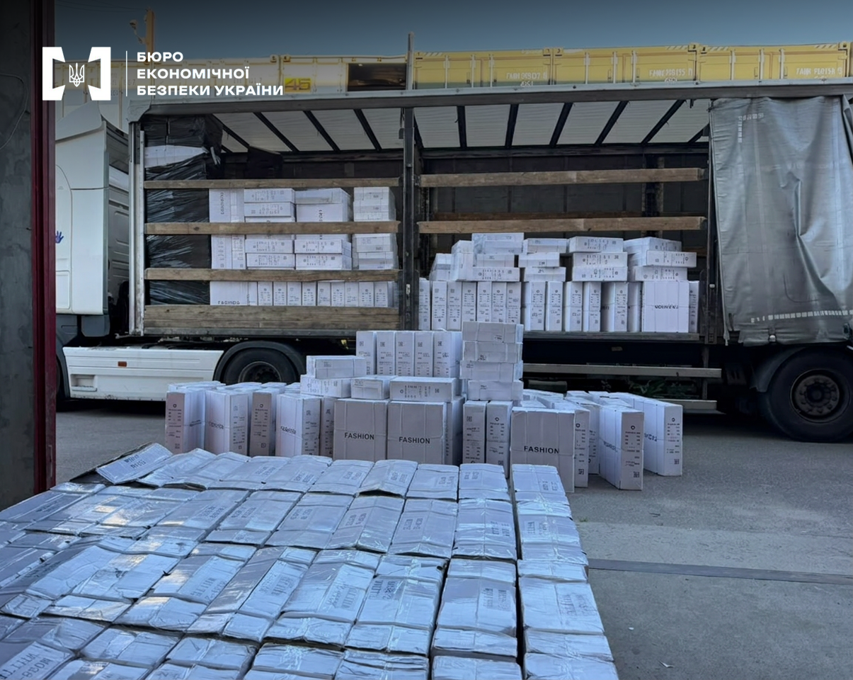 Stacks of white boxes on the asphalt next to the open semi-trailer of a white truck.