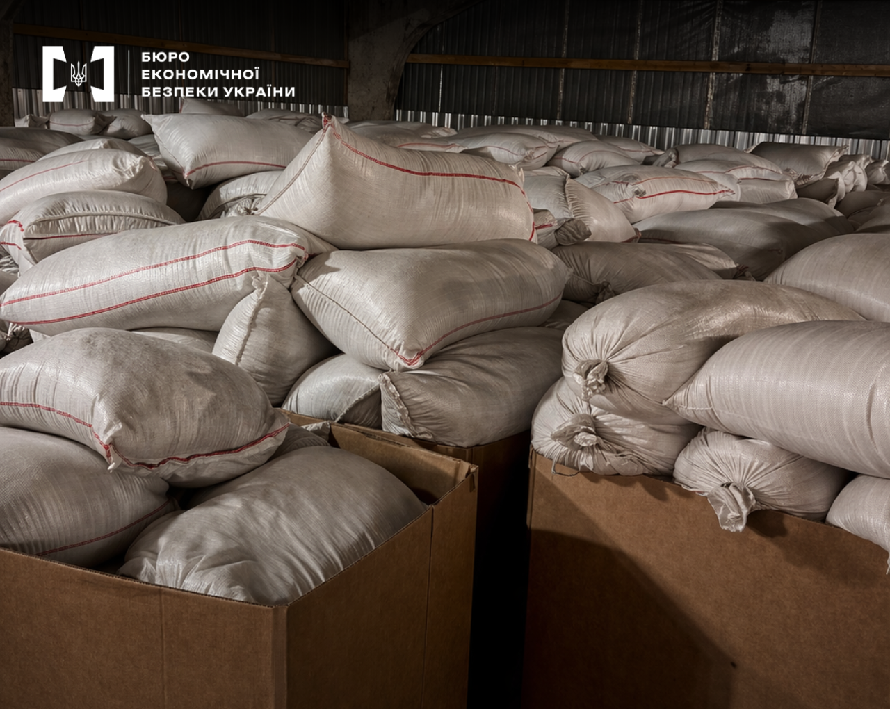 A large pyramid of white sacks with red stripes, loaded into large cardboard boxes in a warehouse.