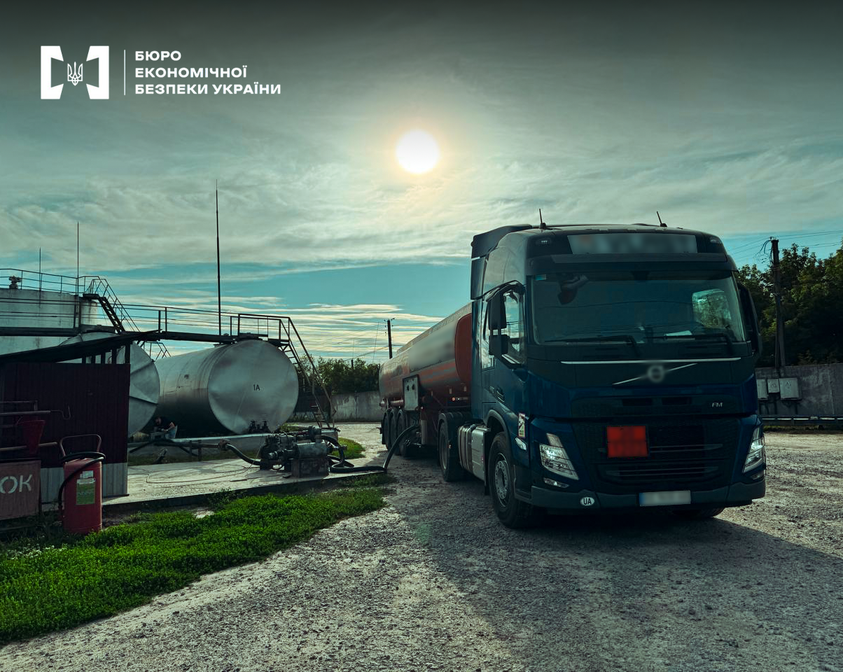 A Volvo fuel tanker truck against the background of large industrial tanks on a sunny day.
