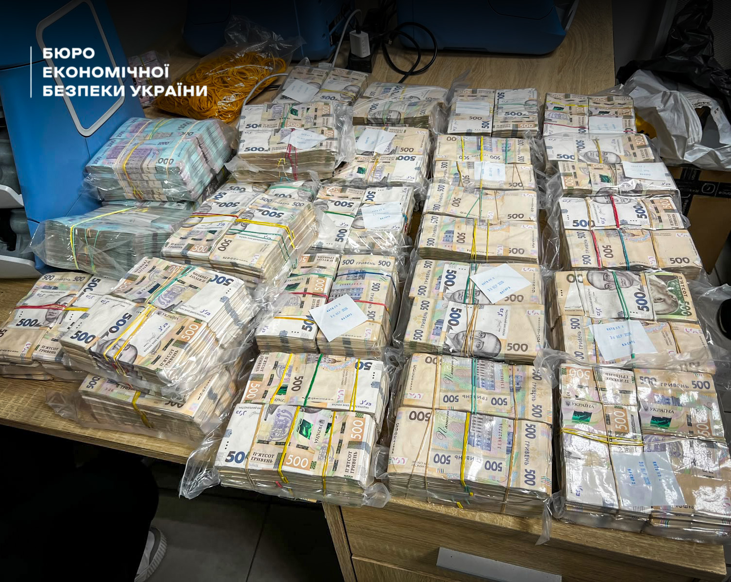 Giant blocks of 500 hryvnia banknotes wrapped in plastic film on a wooden table.