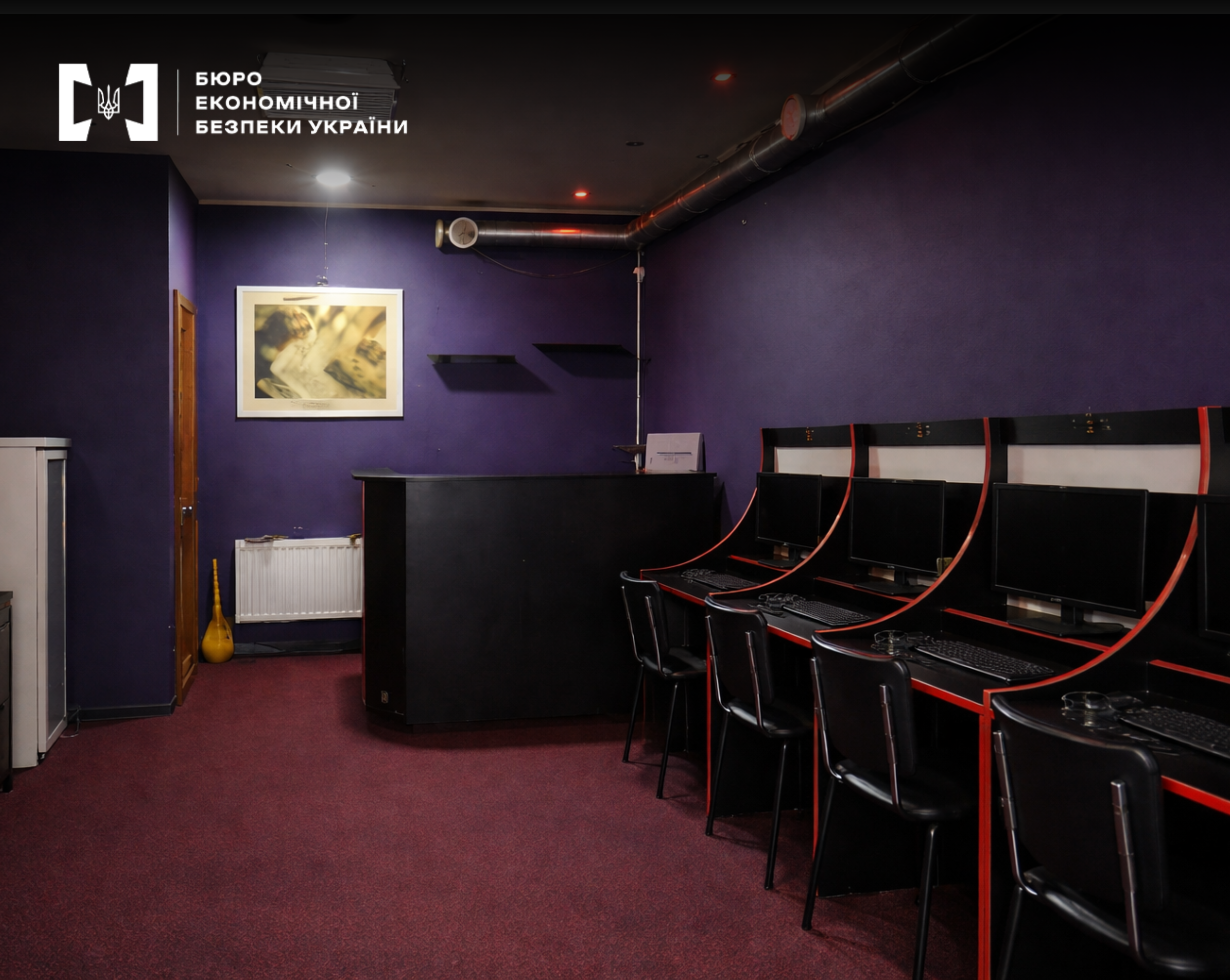 An exposed underground gambling hall with purple walls, a black reception desk, and a row of computers for players.
