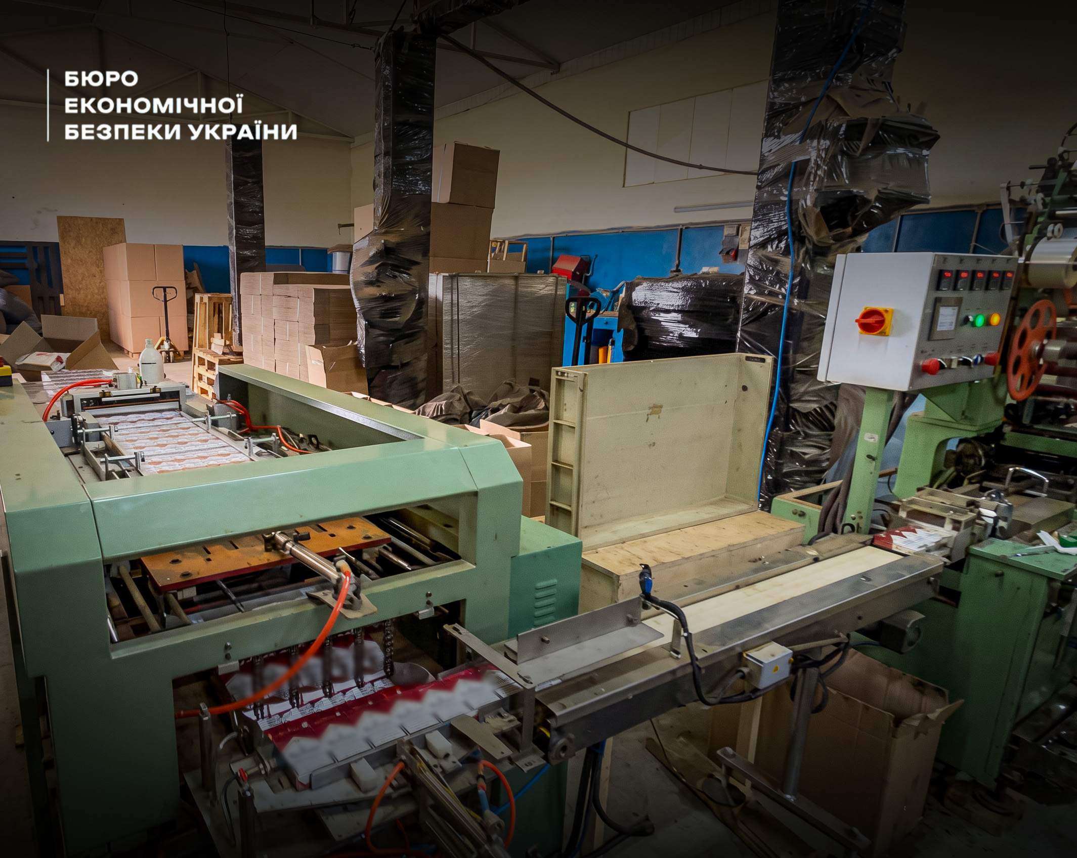 Large green conveyor equipment, packaging belts, and stacks of cardboard boxes in an underground tobacco warehouse.