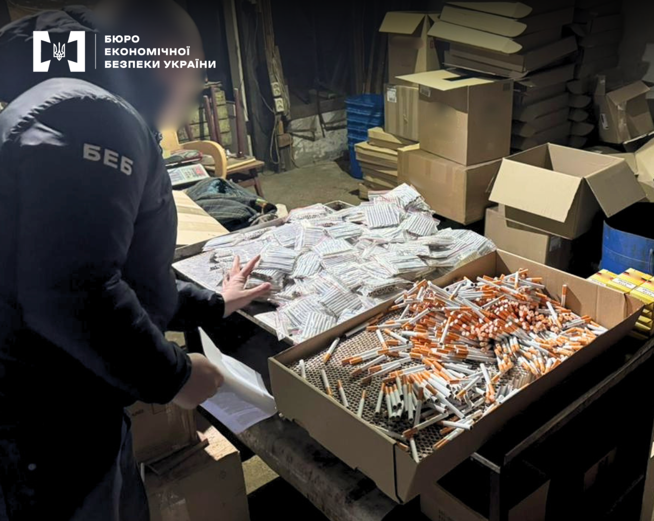 Детектив БЕБ оглядає нелегальний склад тютюнової продукції. В картонних ящиках сигарети насипом або спаковані в зіппакети.