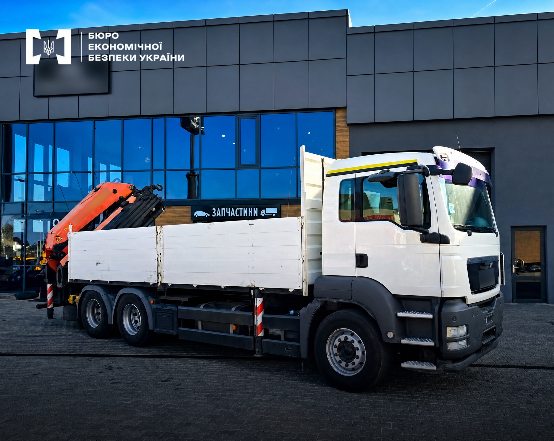 A white MAN truck with an orange manipulator near a building with a sign reading