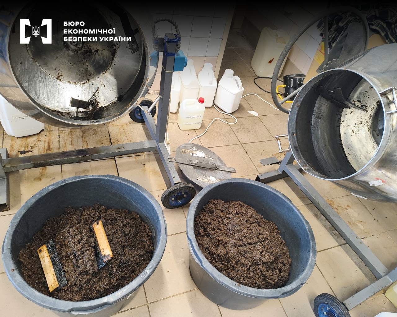 Two large metal drums on wheels next to buckets full of wet tobacco."
