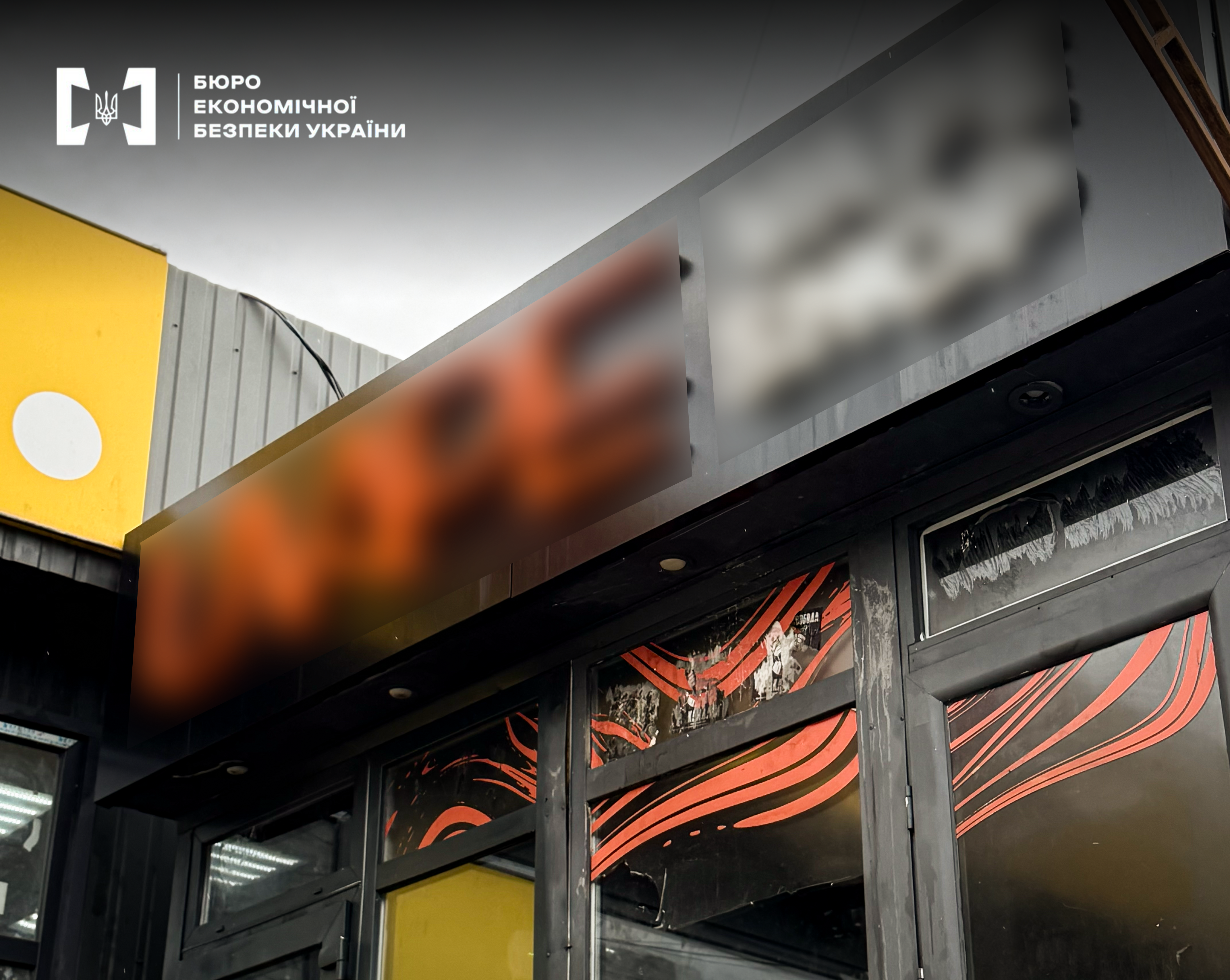 A portion of the facade of a kiosk—a point of sale for excisable goods. The exterior is in dark tones with bright orange accents. The signage is blurred.