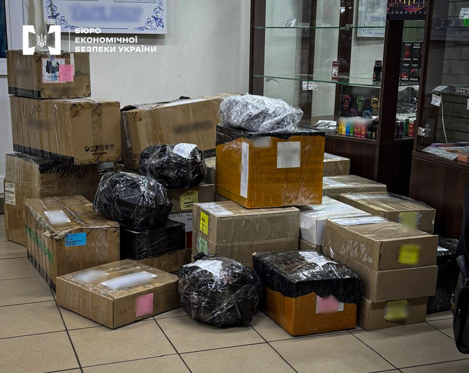 Stacks of mailing boxes and black packages on a tiled floor in a room with display cases.