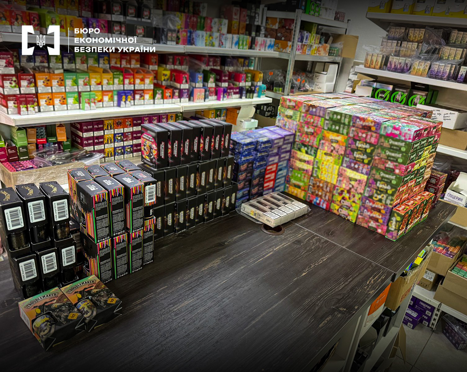 A wooden table covered with packs of electronic cigarettes and small boxes against the background of shelves with goods.