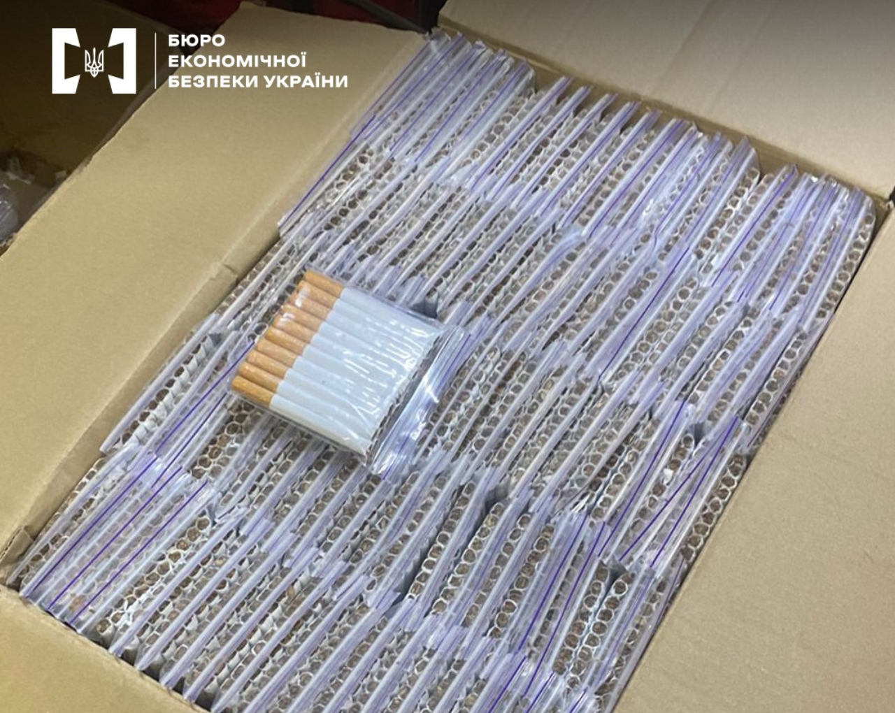 A close-up of an open cardboard box filled to the brim with cigarettes, packaged in zip-lock bags of 20 pieces each