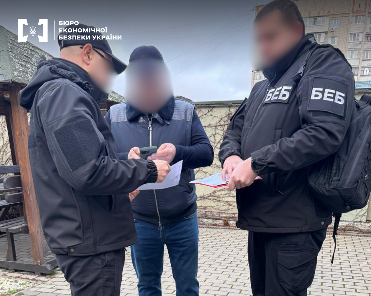 ESBU detectives are conducting procedural actions. One detective is presenting documents to a suspect who is holding a mobile phone
