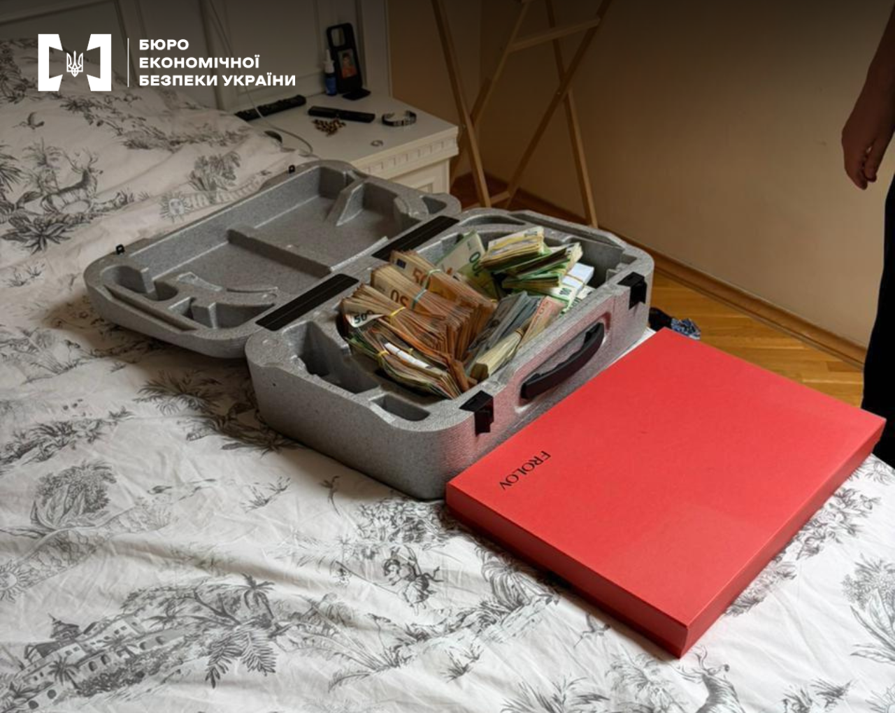 An open gray case filled with bundles of euros and a red FROLOV box on a bed