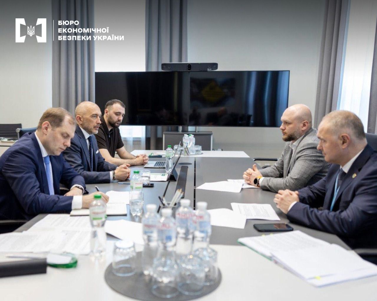 Working meeting between the leadership of the ESBU and the NBU. Five participants in business suits at a gray table against the background of large videoconferencing system screens.