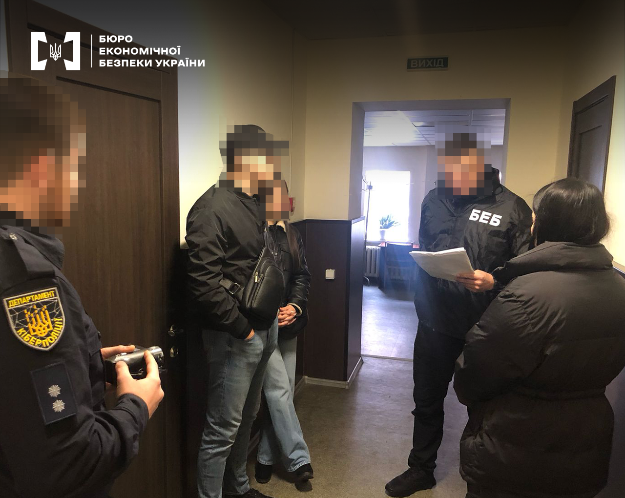Детектив БЕБ оголошує підозру фігуранту справи. Також у коридорі офісного приміщення дві жінки, працівник Департаменту кіберполіції. Обличчя заблюрені