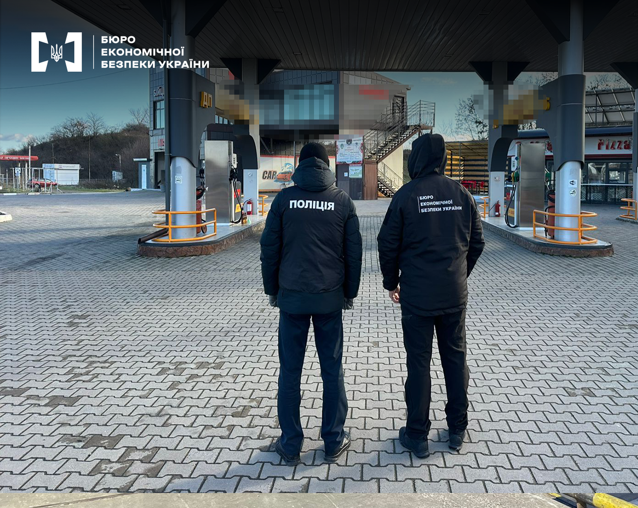 Поліцейський та детектив БЕБ оглядають автозаправну станцію. Територія АЗС з заправними комплексами та приміщеннями. Назва заправки заблюрена.
