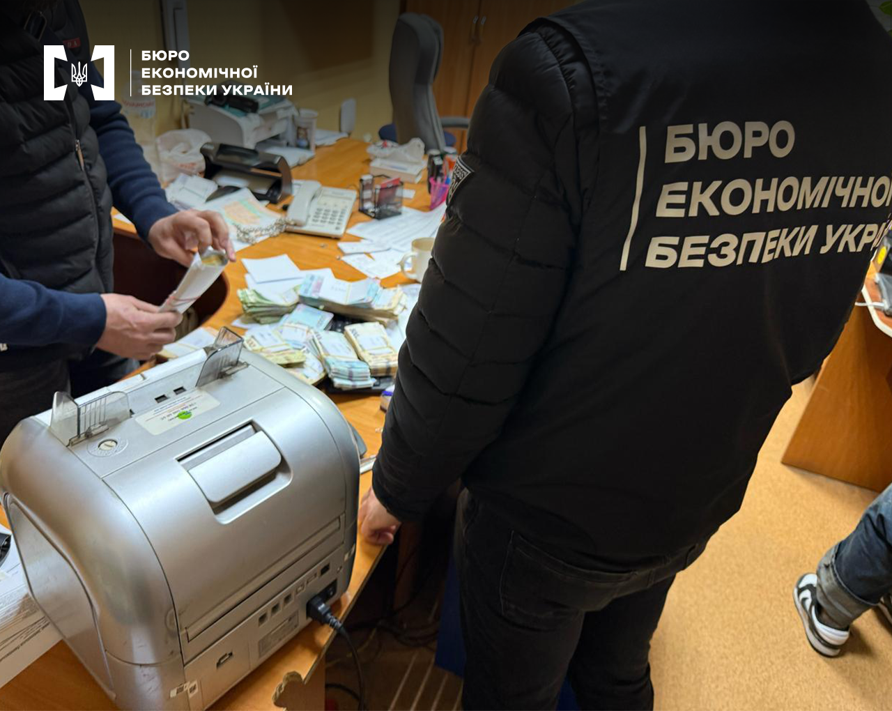 Детектив БЕБ проводить слідчі дії. На столі лічильник банкнот, пачки грошей, документи
