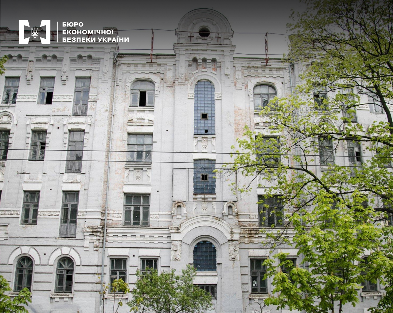 Фасад великої занедбаної сірої будівлі у стилі класицизму з арковими та прямокутними вікнами, присутні елементи ліпнини та архітектурного декору.