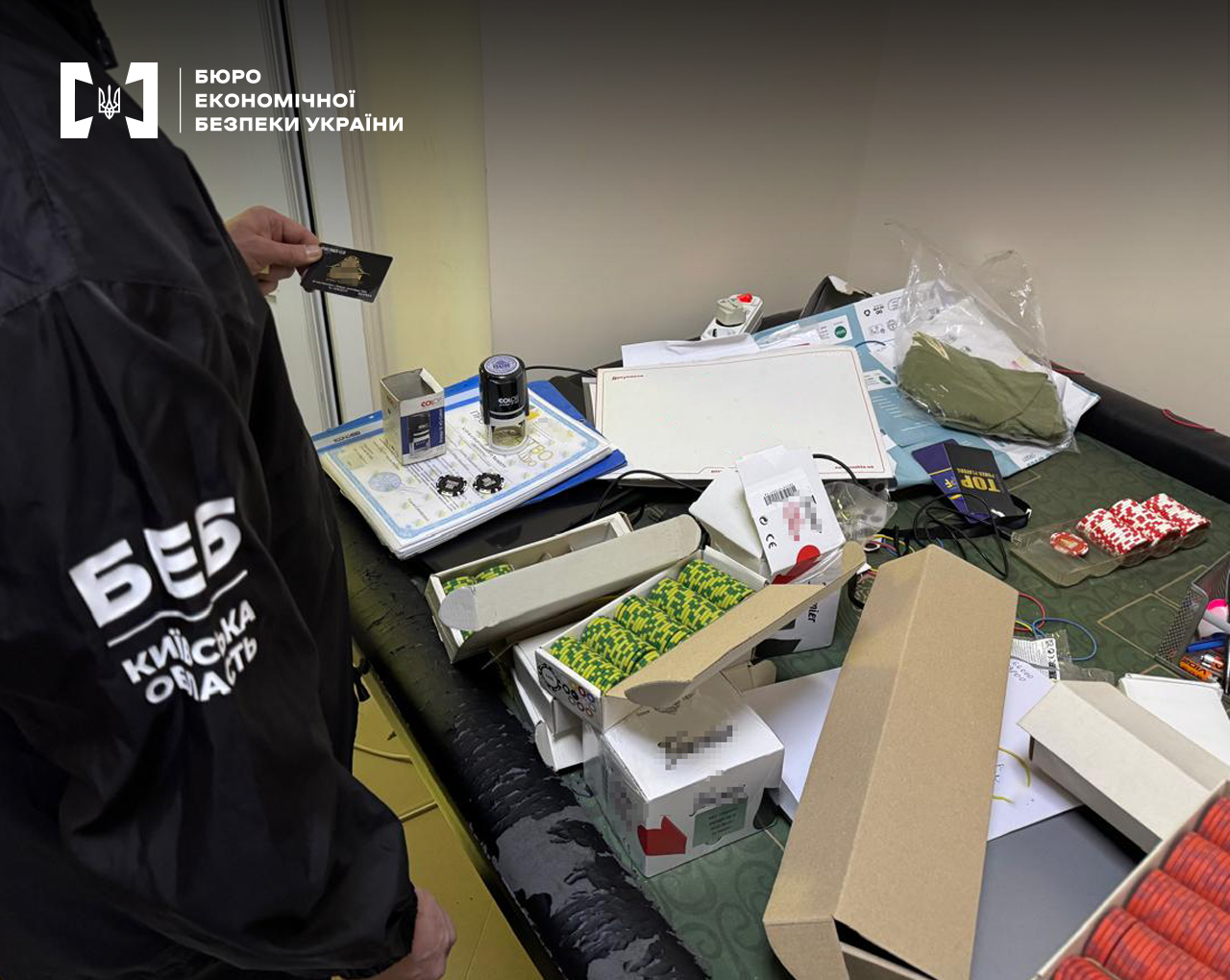 Детектив БЕБ проводить огляд речових доказів, розкладених на столі: документи, печатка, коробки, фішки різного кольору, картки.