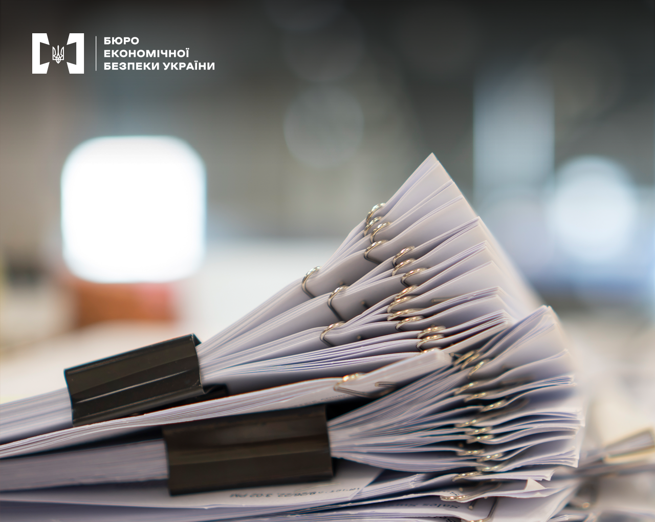 Великим планом стос документів скріплених скріпками та біндерами, фон розмитий.