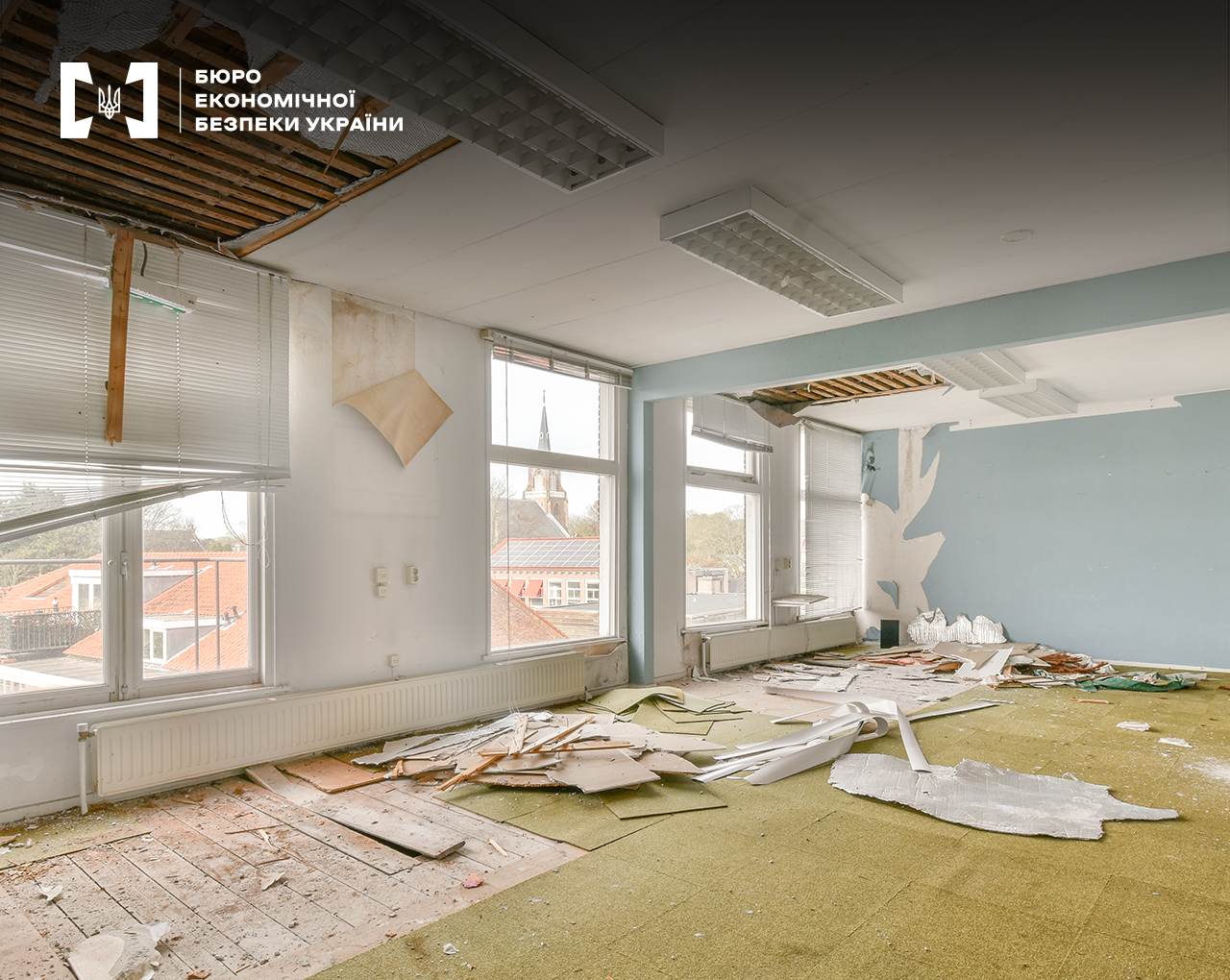 Просторе світле приміщення, що потребує ремонту. Частково зірвані шпалери та ковролін, обвалена стеля, на підлозі будівельне сміття.