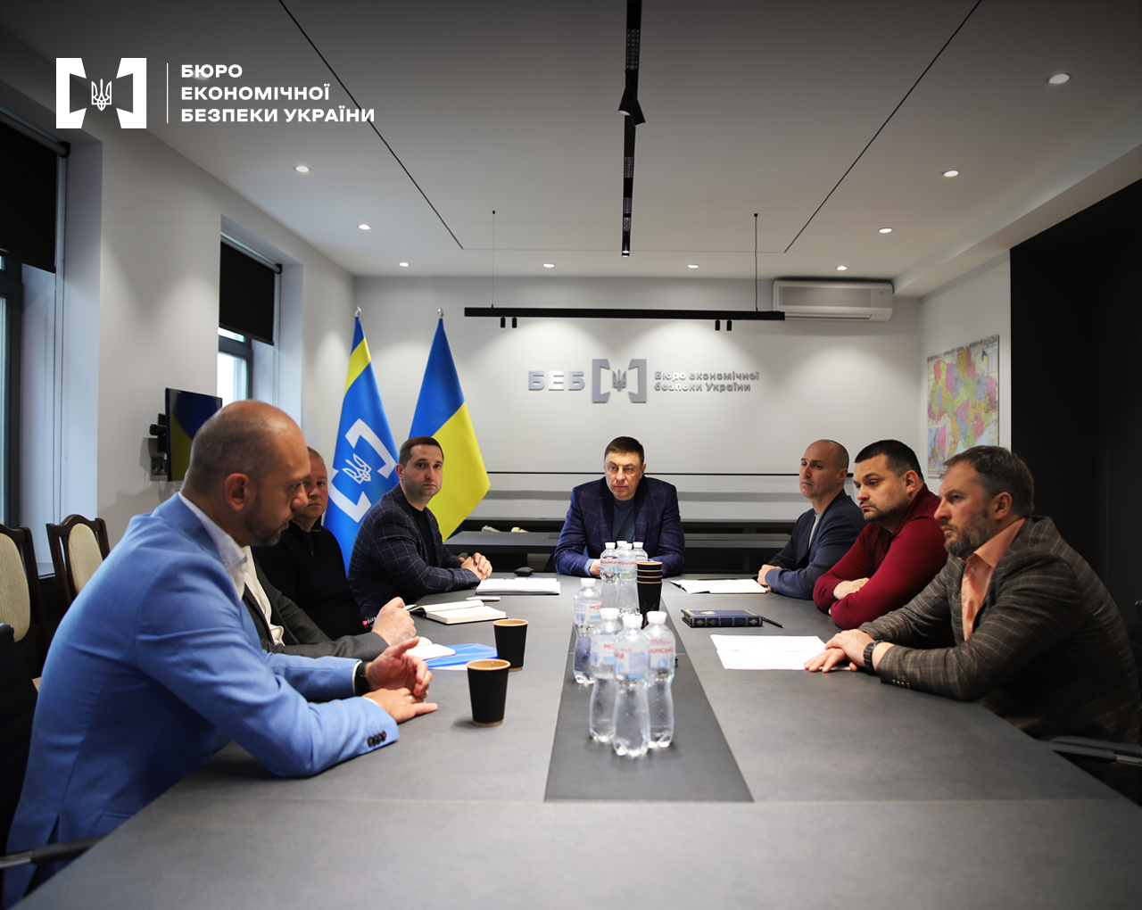 Учасники зустрічі під час обговорення у конференц-залі. На стіні лого БЕБ та напис: «Бюро економічної безпеки України». Поруч прапори України та БЕБ .