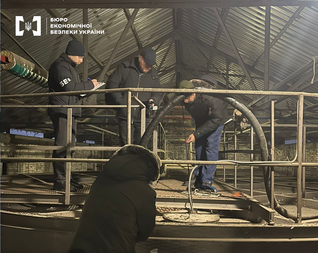 Детективи БЕБ оглядають приміщення заводу з виробництва етанолу. Промислові резервуари, труби, металеві конструкції.